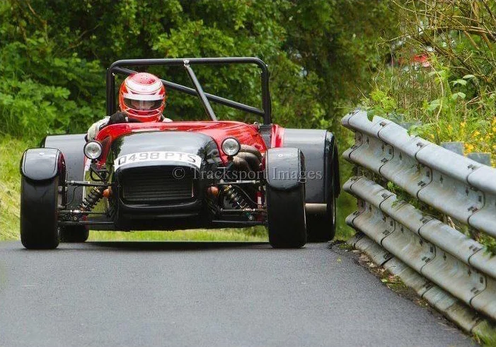 Red Caterham Seven navigating a tight hillclimb corner beside Armco barrier